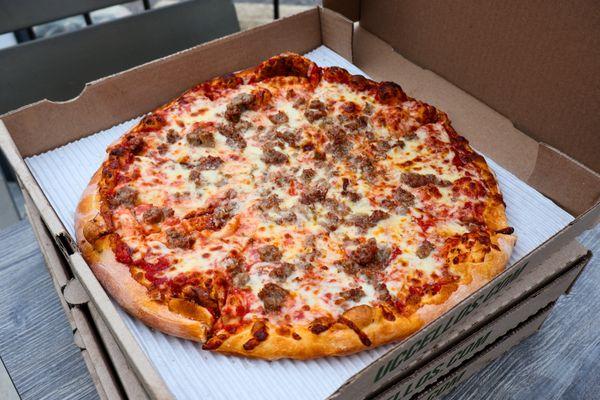 A round pizza with red sauce, melted cheese, and Italian sausage inside an open to-go pizza box...