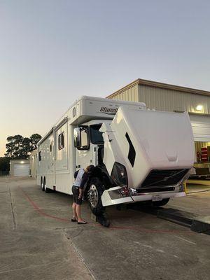 A technician from Redline Wrecker Service inspects a large RV truck with the hood lifted...