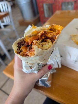 A picture of the bacon breakfast burrito with a few bites taken out of it. The eggs, bacon, tots, and red Chile can be seen.