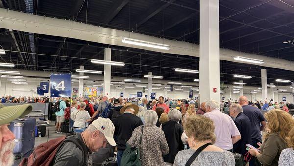 View of mass of passengers weaving in line or looking for their bags. Numbers are on tables with bags.