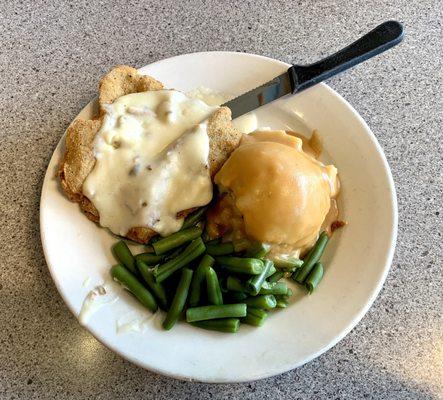 Country fried steak with breakfast sausage gravy on top mashed potatoes with brown gravy and green beans.
