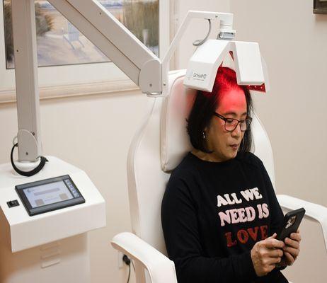 A female patient relaxes and looks at her phone while receiving a treatment with the GetHairMD Clinical Hair Growth Laser.