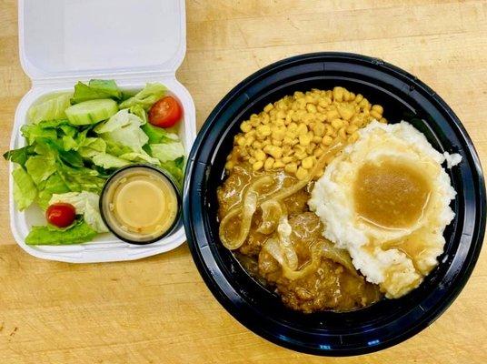 Salisbury steak with mashed potatoes, corn and a garden salad.