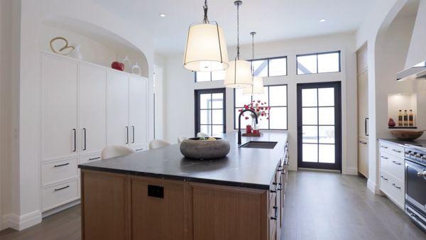 Bright, elegant kitchen with black-framed French doors, a large wood island with dark countertop, and white cabinetry .