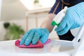 A close-up of a person wearing blue rubber gloves cleaning a white surface. They are using a white spray bottle and a bright ...
