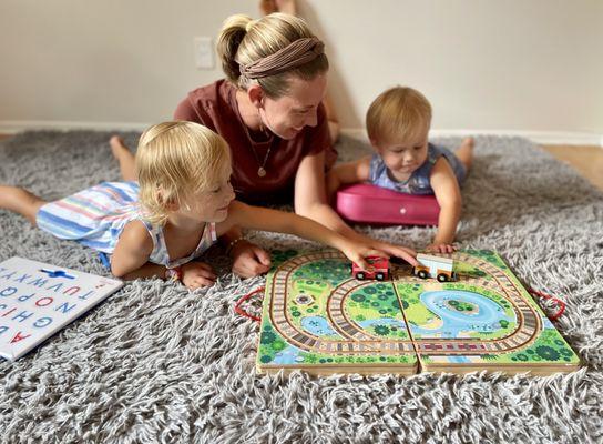 Playing in prone prop and over a wedge while playing with trains on a wooden track to improve fine and visual motor skills and strength.