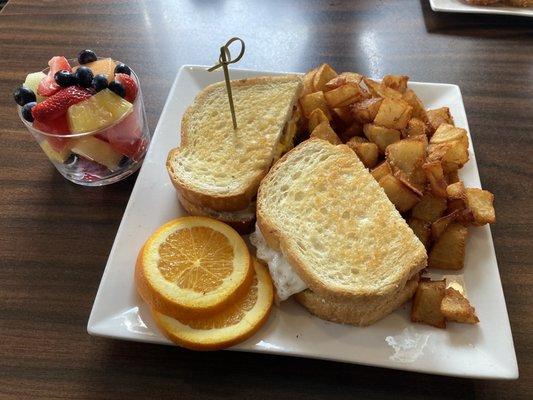 Avocado breakfast melt, fried potatoes, and a fresh fruit cup.