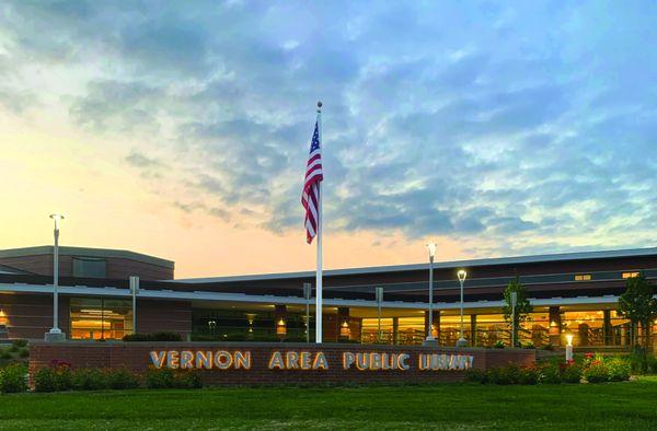 The US flag flies over the library entryway at dusk.