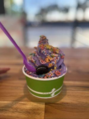 Ube soft serve in cup topped with fruity pebbles, sprinkles, and Oreo.