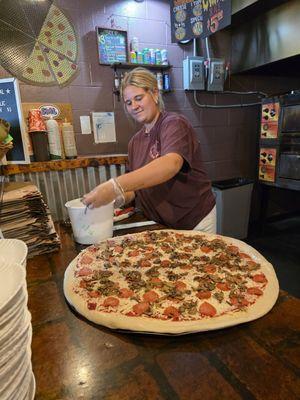 One of the employees making a pizza.