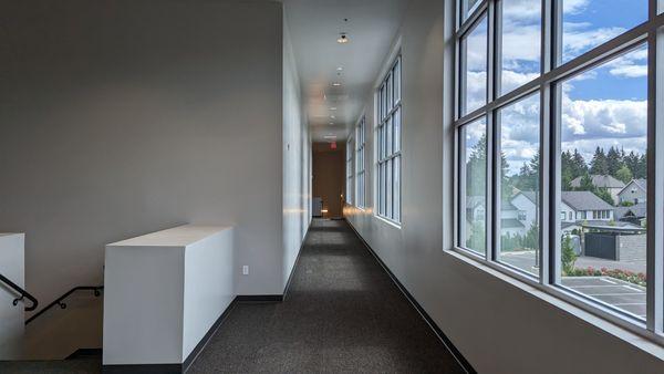 View along a naturally well-lit interior hallway with large glass windows to the right