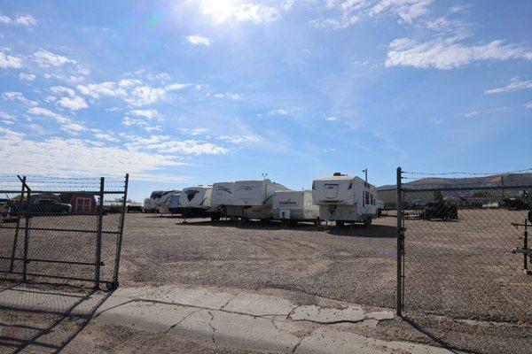 A gated empty lot with asphalt that has some trailers parked in it.