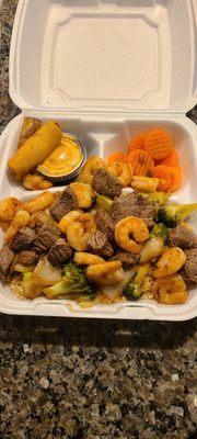 Steak and shrimp meal with a spring roll and sweet carrots.
