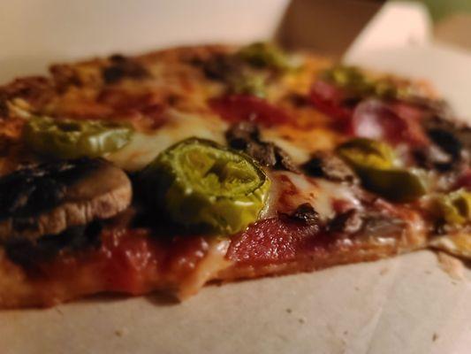 Side-shot of a Medium thin-crust with pepperoni, mushrooms, and jalapeno.