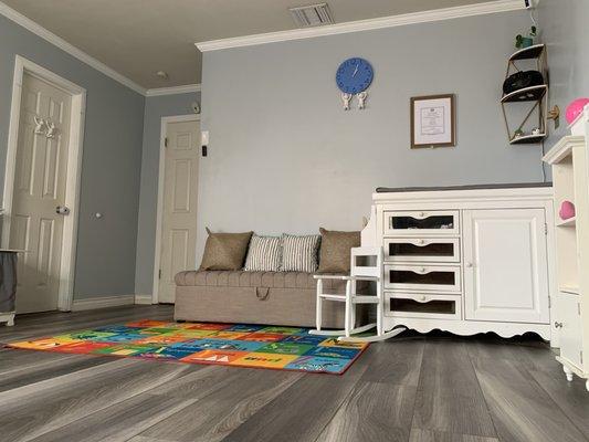 Changing table, rocking chair and ottoman with carpet with a bookshelf where children can sit and read books.