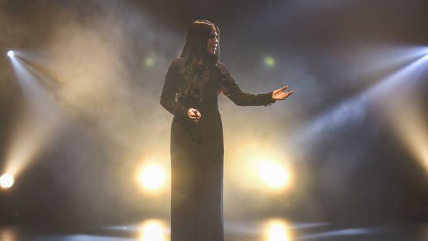 A woman in a black dress performs under dramatic stage lighting, surrounded by fog, creating a cinematic and emotional atmosphere.