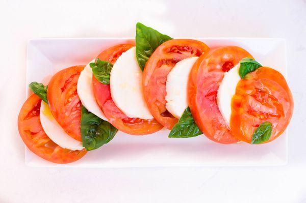 Caprese Salad: fresh mozzarella layered with vibrant heirloom tomatoes, basil leaves, and a drizzle of extra virgin olive oil and balsamic