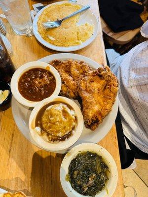 Fried chicken breasts, mashed potatoes with gravy, and greens.