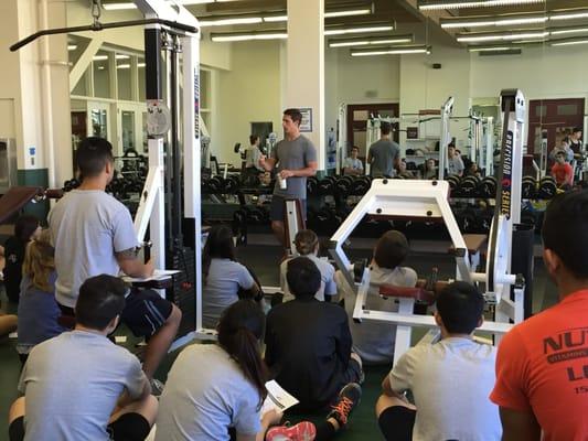 Giving a lecture on the pros and cons of free weights versus machines for various goals