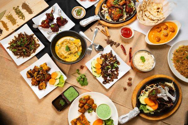 A colorful spread of authentic Nepali and Indian dishes featuring juicy grilled meats, steaming dumplings in sauce, crispy fried snacks.