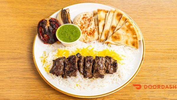Steak kabob with sabzi sauce, hummus, pita, and grilled tomato and onion
