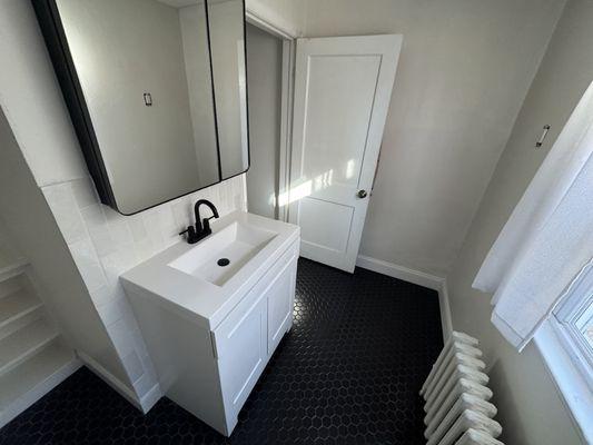 Another after of a new medicine cabinet, vanity sink, new black mosaic hexagon tile with a fresh coat of paint and new white wood trim.