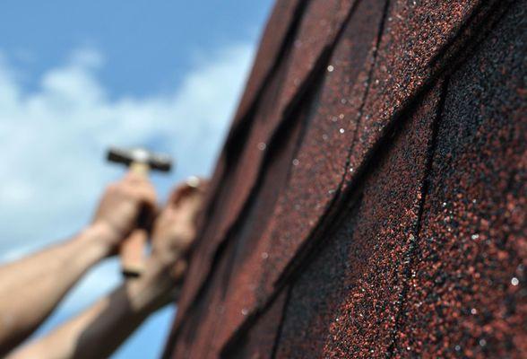 Close-up of new asphalt shingles being installed using a roofing nail gun.
