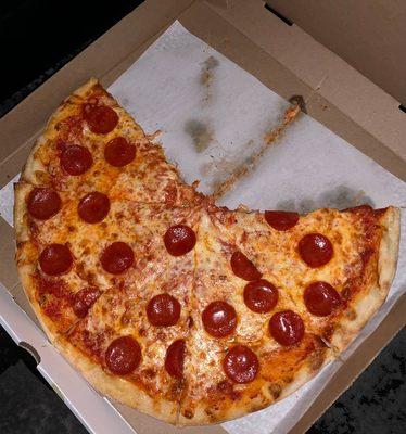 A pizza pie with a few slices missing, topped with many pepperoni's.