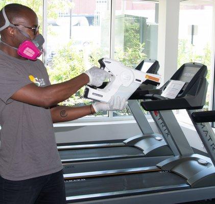 Accusan staff with sanitization equipment desanitizing gym equipment.
