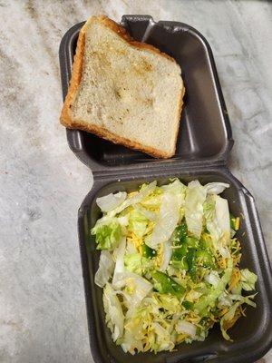 $4 side salad with a 3/4 cup of shredded lettuce with a drizzle of cheese and nothing else. Next to it is a slice of Texas bread.