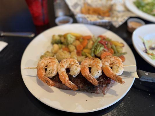 NY steak with a side of shrimp skewers and house veggies.