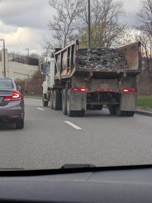 Fabrizio truck with an unsecured load of stone pulling onto a pot hole cover highway.