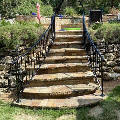 A pair of curved decorative handrails coming down these flagstone steps for these customers to prevent from falling.