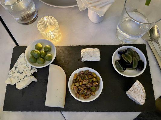 Cheese plate served with bread, grapes, pistachios and green olives.