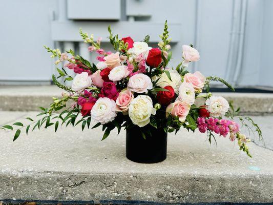 Beautiful red, coral pink, ivory, and blush roses with snap dragons in a black vase