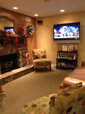 Cozy waiting area with fireplace, leather couch, books and toys for children.