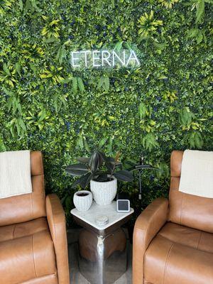 Relaxation lounge at ETERNA Santa Monica featuring leather chairs, lush greenery wall, and a peaceful space for recovery and wellness.