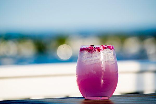 A vibrant pink cocktail sits on a wooden table, its icy contents catching the light of a sun-soaked afternoon.