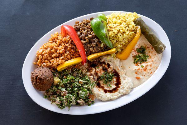 A vibrant Traditional Combo with rice, lentils, tabbouleh, hummus, baba ghanoush, falafel, grape leaf, and fresh veggies.