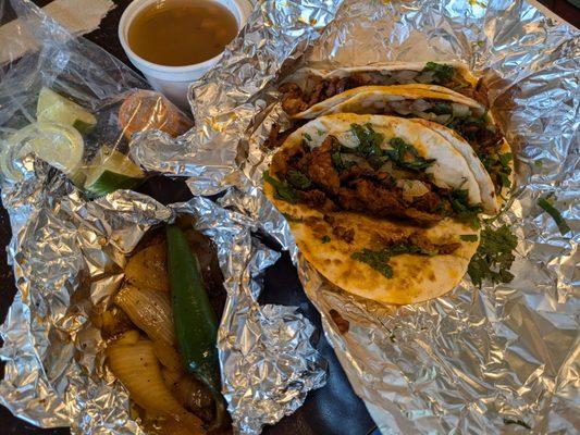 Three tacos al pastor on flour with complimentary beans, onions, pepper, salsas, lime