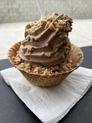 Chocolate soft serve in a waffle cone topped with nuts.