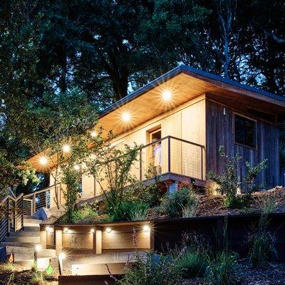 Welcome to our teak ADU, glowing at dusk and surrounded by reforested greenery.