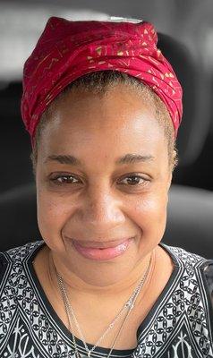 This is my face after Johanna finished my facial. Bright and youthful. Black woman with black and white dress wearing a red head wrap.