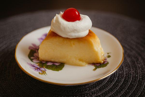 Cream cheese flan with whipping cream topping and cherry on top.