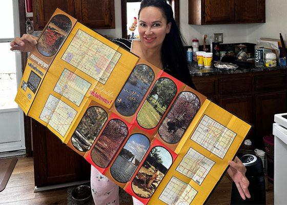 Lisa Christiansen holding the 1969 Okla. State map featuring her childhood home while standing in her childhood home
