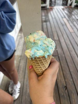 Single scoop of birthday cake ice cream on a waffle cone