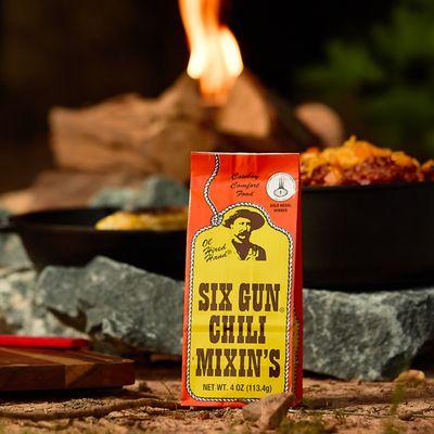 Bold packaging of Six Gun Chili Mixin's sits by the campfire, ready to bring cowboy comfort food to life under the open sky.