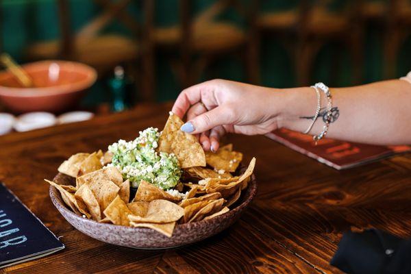 Guacamole dip with cotija cheese sprinkle on top served with corn tortilla chips.