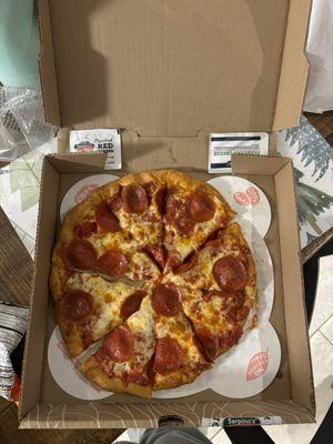 Small pizza in box with a crushed red pepper packet and Parmesan cheese packet