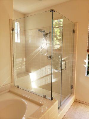 Corner framless shower door with a tub on one side . Shower door with wall mount hinge in chrome finish.